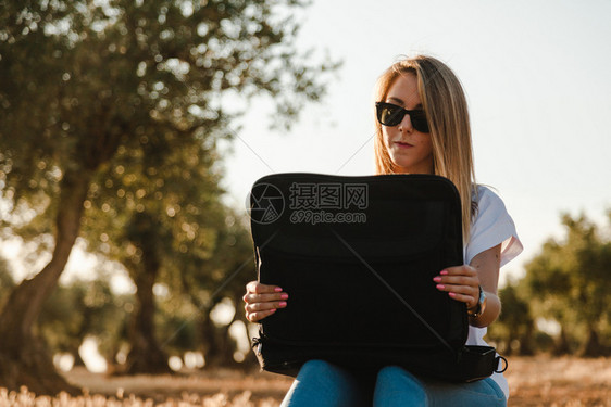 坐在橄榄树田里的拥有笔记本电脑的年轻妇女正面一种树叶图片