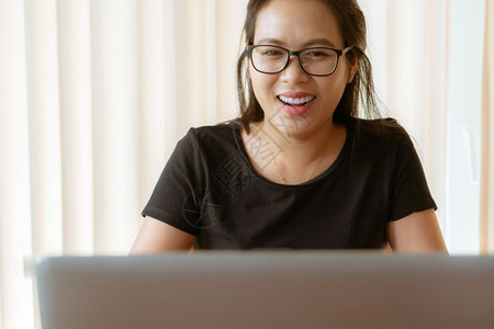 使用膝上型笔记本电脑的年轻亚洲妇女坐在家中做笔记本工作的年轻亚洲妇女社会的联网获得图片