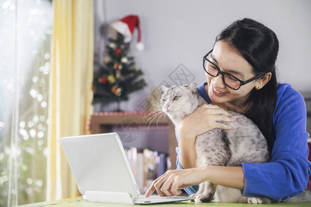 女士专业的微笑使用笔记本电脑与视频话连线美丽的女在看摄影机朋友的视频电话和在家休息的可爱猫聊天时讲话校对Portnoy图片