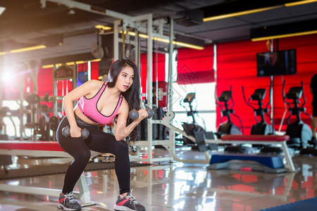 亚洲女在体育健身室内运动和俱乐部中进行有哑铃运动的锻练训并配有运动设备体操背景的健身俱乐部亚裔妇女身体力量活动图片