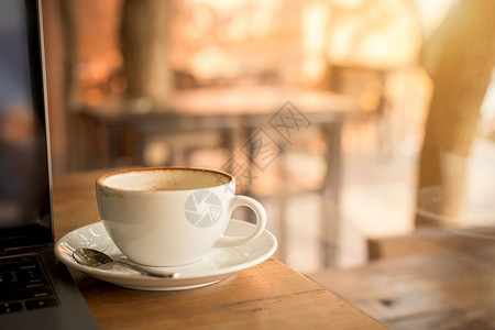 在咖啡厅店的木制办公桌上柜台在商业工作构想期间用杯和膝上型计算机关闭热咖啡拿铁与艺术牛奶泡沫笔记本电脑现代的木头图片