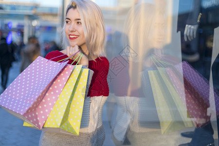消费主义时髦的美丽女孩拿着购物袋看照相机和微笑容购物者图片