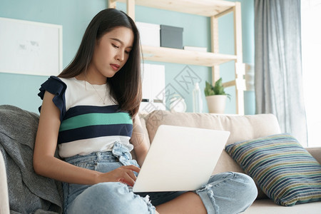 成人室内的部在家中客厅沙发上坐着电脑膝型笔记本电脑的女青年早上做打字工作的Asian女孩她在家里工作图片