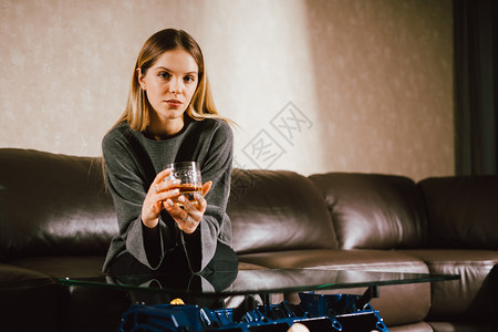 年轻的caucasian金发年轻女孩坐在沙地上豪华屋内拿着威士忌杯子特制V8车引擎桌时装照片和美丽的笑容金属保持感的图片