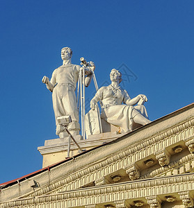 女在白俄罗斯大林时代风格的明斯克工会宫屋顶上男子雕刻着有花粉和坐在妇女着的男子雕塑户外宽慰图片