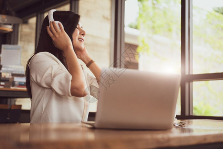 店铺成人现代的快乐亚洲妇女在咖啡店以电脑笔记本和生活方式概念自由与户外工作场所为主题放松娱乐并聆听咖啡店里的音乐图片