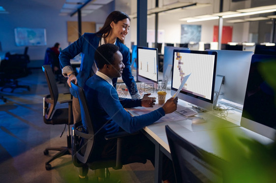 中央电脑两位在夜间办公室工作的快乐经理男女工人背景为深色商务中心内部现代工作场所两位在夜间办公室工作的快乐经理图片