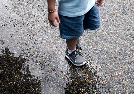 湿的亚裔小孩腿在街上泥坑里走过水乐趣图片