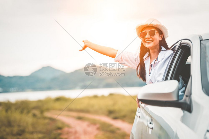 微笑喜悦自然快乐的女子在开窗车外手挥有草地和山湖背景的草地和山湖背景人们在度假旅行中以者身份享受轻松的生活方式交通和旅行概念图片