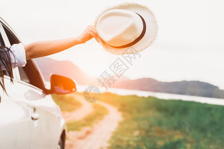 运输保持外部快乐的女士手握着帽子在开窗车外戴有草地和山湖背景的草地和山湖背景的帽子人们在假期旅行时享受放松的生活方式图片