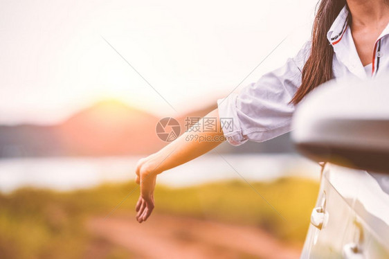 天空畅快户外乐的女子在开窗车外手挥有草地和山湖背景的草地和山湖背景人们在度假旅行中以者身份享受轻松的生活方式交通和旅行概念图片