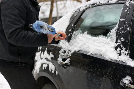 霜城市清除冬季雪汽车冬季问题一个穿着黑色夹克和手套的男人明显手在特殊的刷子帮助下用它把车从雪中打扫干净图片