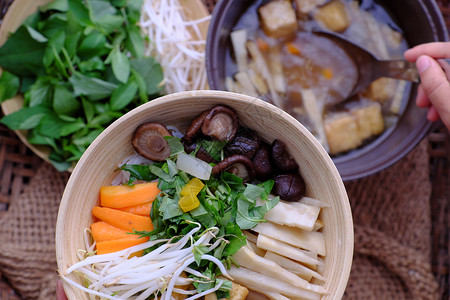 妇女用手从汤锅中勺子准备食物早餐包干草碗竹鱼面和豆腐蘑菇羊叶草药蔬菜的简单但素食可口亚洲越南生的图片