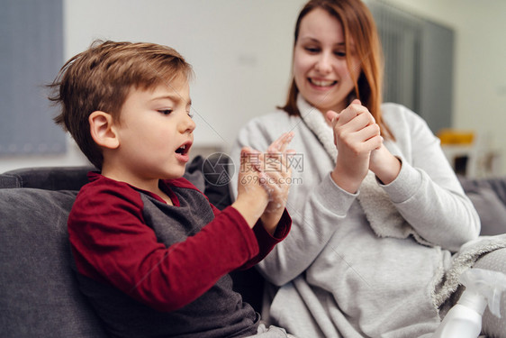 坐在沙发床上的母亲用酒精消毒剂和孩子洗手消毒图片