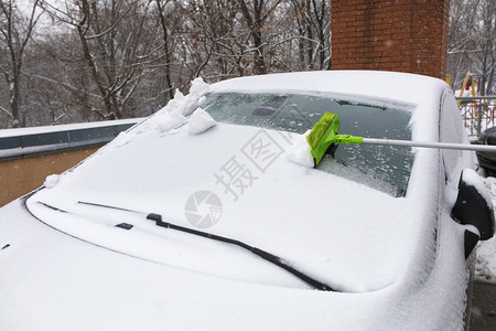 雪堆栏杆长折叠的绿刷子从车挡风玻璃上扫雪在车挡风玻璃上用长的刷子雪复制图片