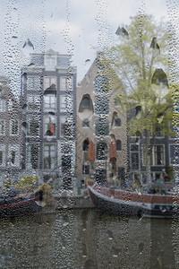 城市的传统屋顶荷兰位于阿姆斯特丹的运河堤岸雨天下来自高点的住宅驳船和真正的荷兰房屋透着窗户通过阿姆斯特丹运河上的雨窗透过一个有滴图片