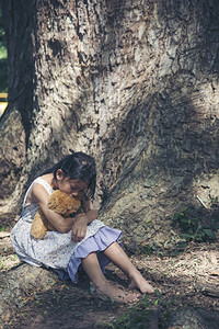 情感保护独自坐在绿公园的树下孤单悲伤地坐在树下寂寞感到悲哀不快乐的女孩在户外拥抱最好朋友玩具自闭症儿童泰迪熊的家庭暴虐焦虑图片