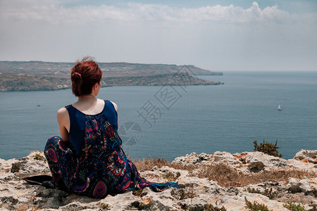 地平线坐在悬崖边缘的红发年轻女人身着顶骨向远海看白种人红发女郎图片