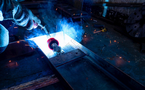 织物气体保护的焊工用氩弧机接金属并产生火花一名男子戴防护手套工业作场所的安全焊工与人在钢铁厂作图片