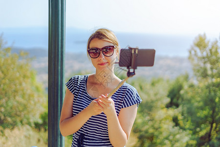 穿着暑期服装的年轻女子使用自相棒和智能手机在海上山拍照同时旅行于秋夏或天在季游客幸福九月图片