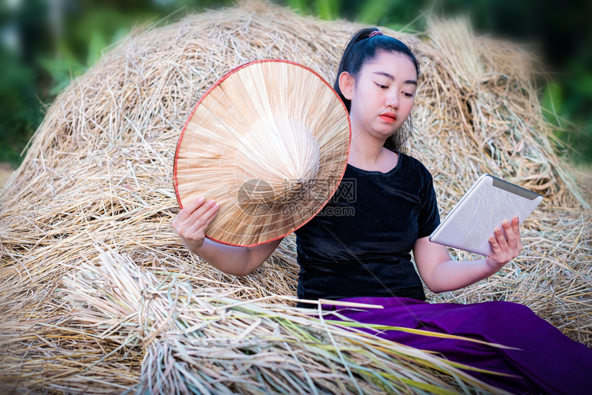 坐在稻草背景的田里时使用数字片子的纵向女农民泰国村景点在泰国种植园帽子有机的图片