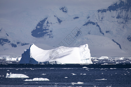 尤其远的地平线大冰山在一片美丽的光亮心情下游在满是雪的黑暗山峰前图片