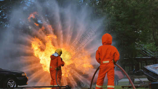 战斗机消防员用水管化学泡沫喷洒剂发动机与火焰战斗的消防员Fierman戴硬帽身穿防火灭器方面的营救训练制服消防队员斗争图片