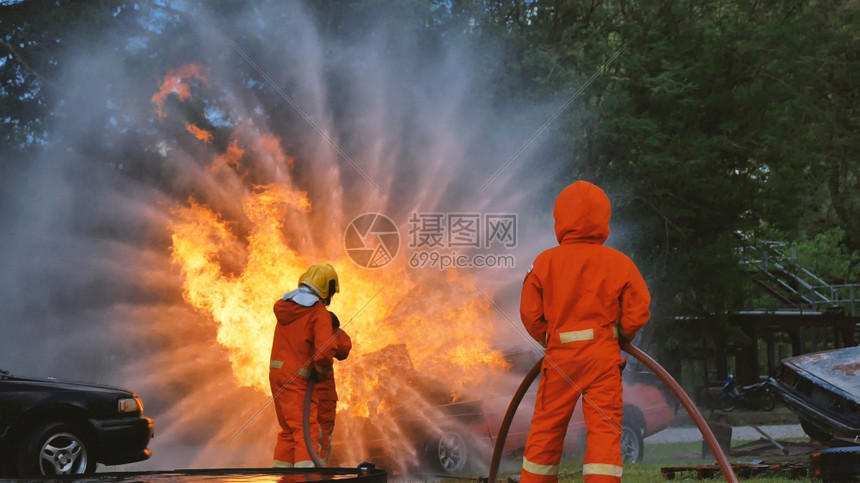 战斗机消防员用水管化学泡沫喷洒剂发动机与火焰战斗的消防员Fierman戴硬帽身穿防火灭器方面的营救训练制服消防队员斗争图片