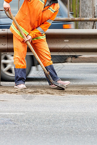 垂直的一位身穿亮橙色反光制服的道路工人铲沙并清除道路上的碎屑垂直图像复制空间道路服务人员用铲子刮掉堆积的沙和碎屑垂直图像职业人行图片