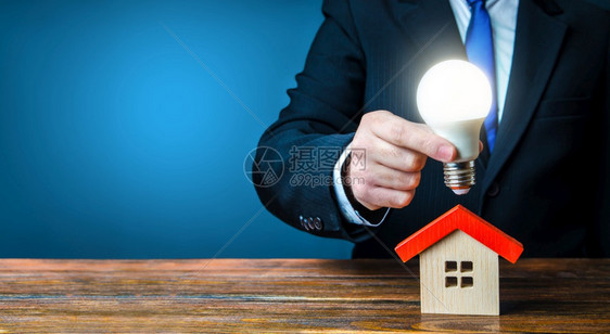 男人在房子模型上方拿着一个发光的灯泡图片