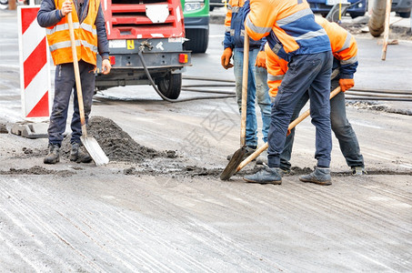 城市的移动身着橙色工作服的道路人用铲子从道路上的旧面铲除杂物道路工人正在铲上的旧面复制图片