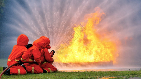 面具救援消防员用水管化学泡沫喷洒剂发动机与火焰战斗的消防员Fierman戴硬帽身穿防火灭器方面的营救训练制服工作图片