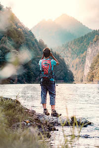 站立带着背包的年轻旅游者在山峰上看望远镜站在河边的岩石上男孩在山度假与背包一起游荡他穿着运动夏季服装笑声波兰男人图片