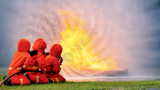 热的消防员用水管化学泡沫喷洒剂发动机与火焰战斗的消防员Fierman戴硬帽身穿防火灭器方面的营救训练制服团队斗争图片
