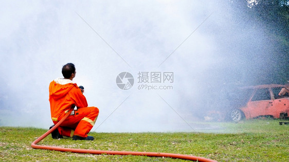 为了救援紧急情况消防员用水管化学泡沫喷洒剂发动机与火焰战斗的消防员Fierman戴硬帽身穿防火灭器方面的营救训练制服图片