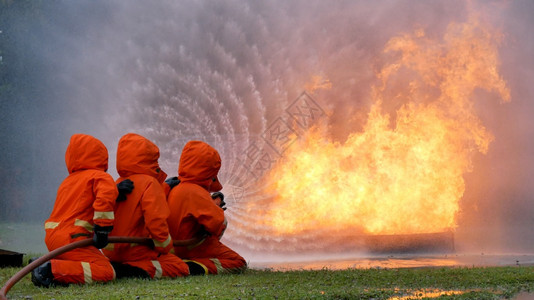 消防员用水管化学泡沫喷洒剂发动机与火焰战斗的消防员Fierman戴硬帽身穿防火灭器方面的营救训练制服战斗机抽烟英雄图片