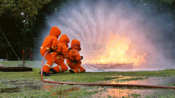 消防员用水管化学泡沫喷洒剂发动机与火焰战斗的消防员Fierman戴硬帽身穿防火灭器方面的营救训练制服英雄工作氧图片