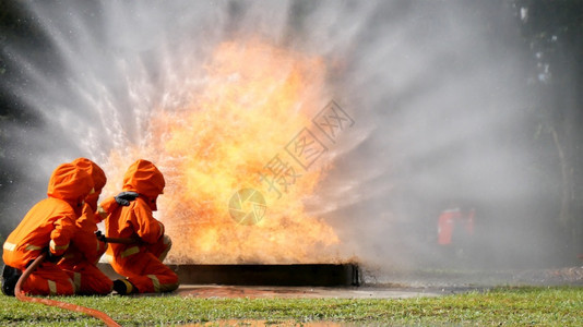 难的氧消防员用水管化学泡沫喷洒剂发动机与火焰战斗的消防员Fierman戴硬帽身穿防火灭器方面的营救训练制服危险的图片