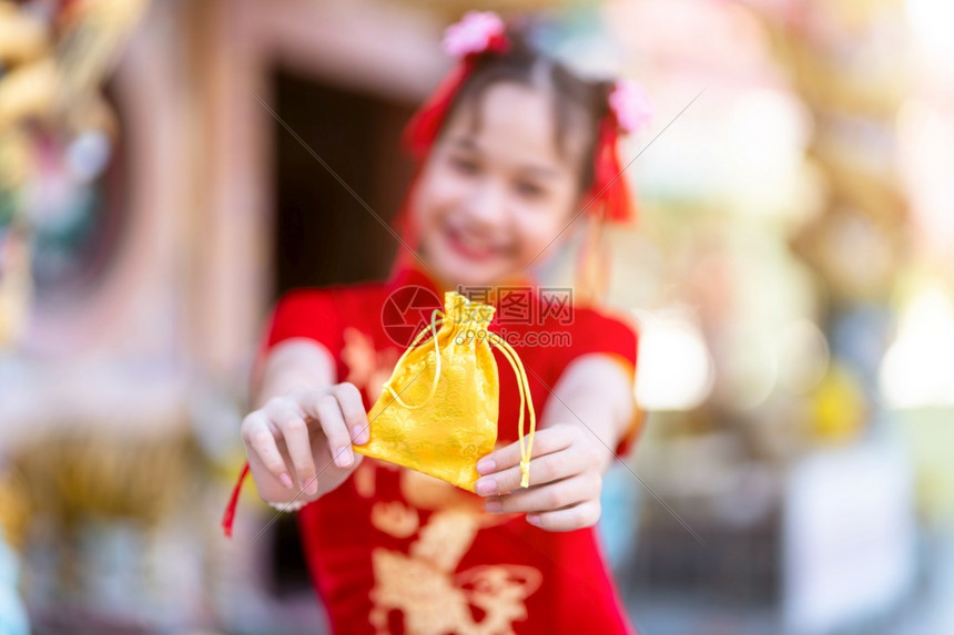 保持快乐的微笑穿着红色传统青山装饰焦点的亚洲小可爱女孩在泰兰神庙举办新年庆典展示金钱袋以备新年盛会时使用图片
