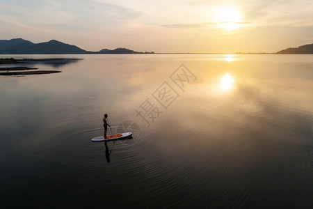 天线太阳日落时站在平坦温暖宁静的河流上划桨板空中景象积极户外图片