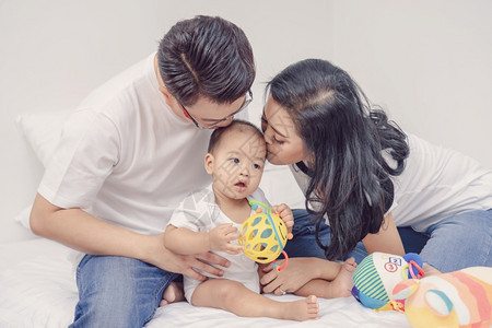 卷曲亚洲幸福家庭的环境父母亲吻男孩婴儿在卧室的家庭生活方式概念中女孩屋图片
