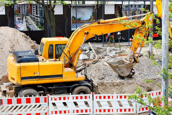 技术的重改造型建筑挖掘机在有围栏的建筑工地上作为城市公用事业挖沟重型道路掘机在建筑工地挖沟图片