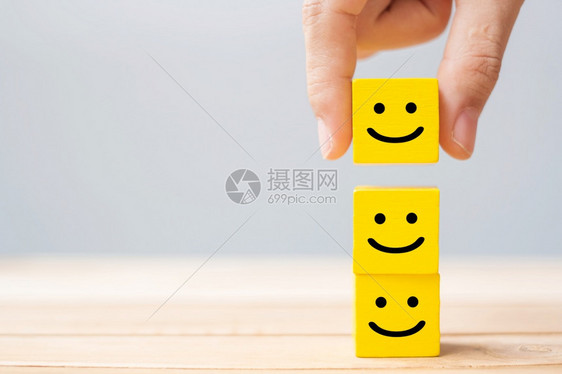 双手在黄色木立方块上手持微笑的面容符号情感服务评级排名客户审查满意度和反馈概念评估天爱图片