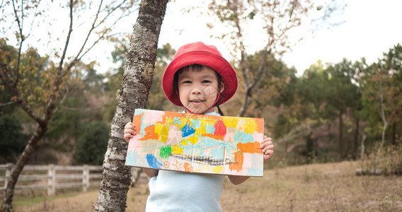 学前班染色快乐的小女孩展示她彩色工作在花园的纸板上俏皮图片
