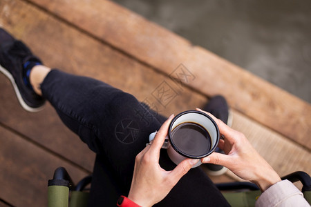一个女孩坐在木码头上手里拿着一杯金属咖啡靠近湖边顶视图空白的一次树叶图片