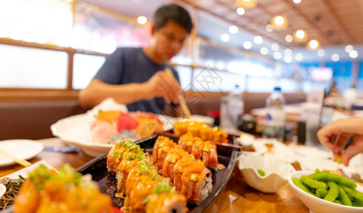 开胃菜派对美食有选择地关注日本餐馆的食本餐厅沙门寿司在一块盘子上有日本食品而餐盘上的模糊男子在餐厅健康亚洲食品沙门寿司菜单中用筷背景图片