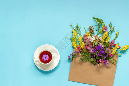 母亲蓝色的好手工艺品袋和一杯草药茶中花地多彩的生锈古花朵蓝绿背景的香草茶在手工艺品袋和草药茶杯中的花朵图片