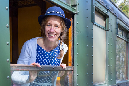 穿着蓝色旧式衣服的高加索中年妇女在蒸汽列车窗上服装机微笑图片