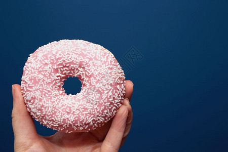 吃冰镇手拿着一个美味的彩色甜圈在深蓝色背景附近洒水糖概念手拿着一个美味的彩色粉甜圈糖概念丰富多彩的图片