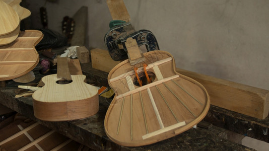 仪器两把木吉他正在组装过程中压机将零件固定在木匠工作台上背景是灰色的墙壁两把木吉他正在组装过程中压机将零件固定在木匠工作台上优质图片